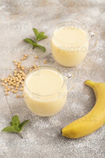 Organic non dairy banana and soy milk in glass on brown concrete background. Vegan healthy food concept, side view, close up
