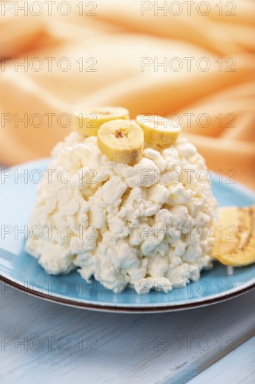 White ?ottage cheese, Curd, with Banana on blue wooden background and orange textile, side view, close up, selective focus