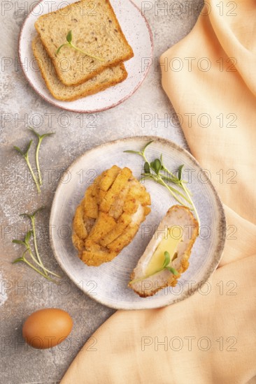 Chicken Schnitzel on blue plate with microgreen on brown concrete background and orange linen textile. top view, flat lay, close up