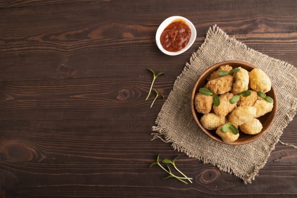 Fried crispy Chicken Nuggets with ketchup, microgreen on brown wooden background and linen textile. top view, flat lay, copy space
