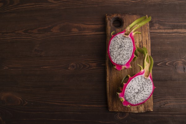 Ripe Pitaya on cutting board on brown wooden background, top view, flat lay, copy space, minimalism