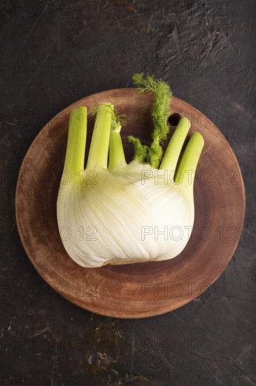 Fresh Fennel bulb on wooden cutting board on black concrete background, top view, flat lay, copy space, minimalism