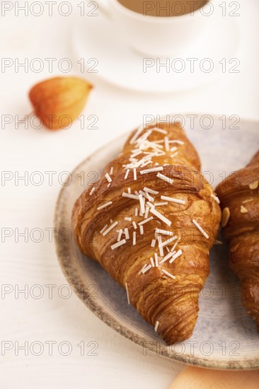 Croissant on blue plate on white wooden background and orange linen textile, cup of coffee, side view, close up, selective focus