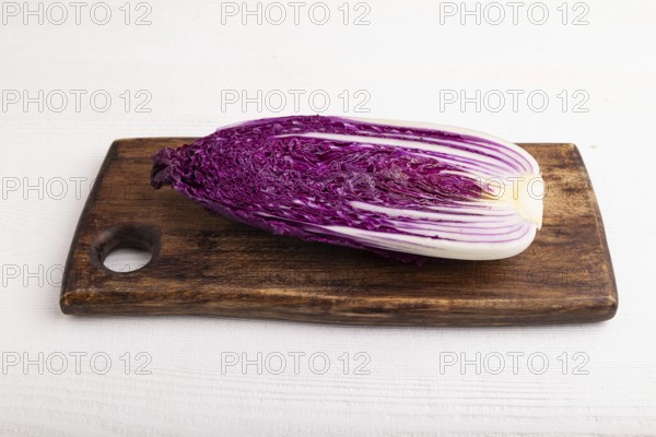 Purple Chinese cabbage on cutting board on white wooden background, side view, close up, minimalism