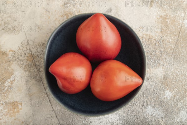 Red Heart shape tomatoes in blue bowl on brown concrete background. Top view, copy space, flat lay. healthy food, vegetable, minimalism