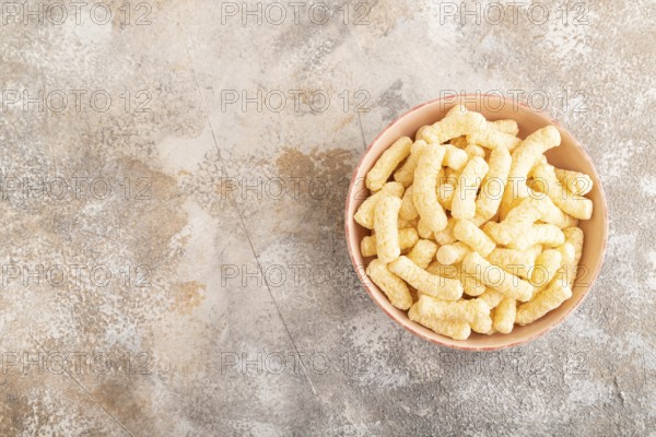 Corn flakes sticks with caramel in ceramic bowl on gray concrete background. Top view, flat lay, copy space