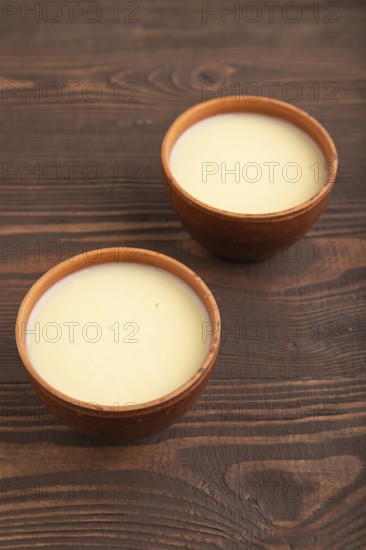 Organic non dairy banana and soy milk in clay cup on brown wooden background. Vegan healthy food concept, flat lay, side view, close up
