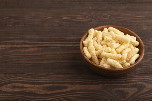 Corn flakes sticks with caramel in wooden bowl on brown wooden background. side view, copy space