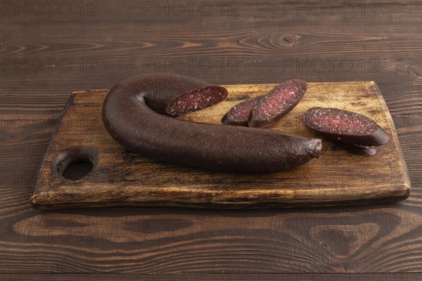 Sujuk sausage on wooden cutting board with pepper and herbs on brown wooden background. Side view, close up