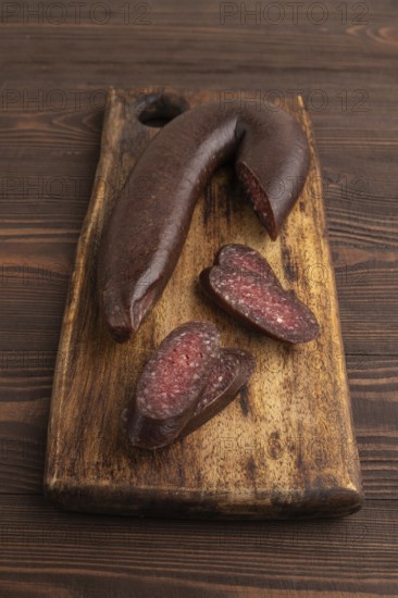 Sujuk sausage on wooden cutting board with pepper and herbs on brown wooden background. Side view, close up
