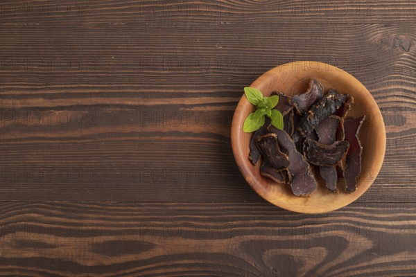 Armenian Basturma dried meat on wooden bowl with pepper and herbs on brown wooden background. Top view, flat lay, copy space