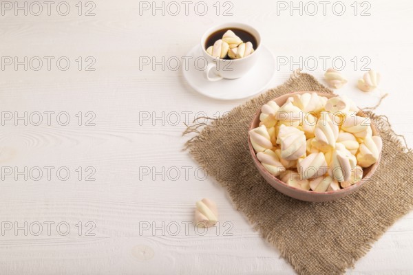 Orange and pink marshmallow in ceramic bowl on white wooden background and linen textile, side view, copy space, minimalism