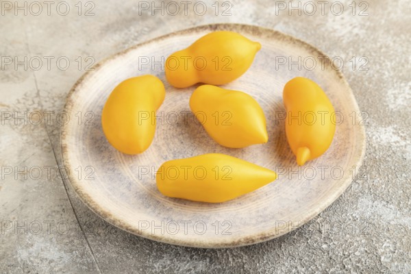 Yellow tomatoes on plate on brown concrete background. Side view, close up. healthy food, vegetable, minimalism
