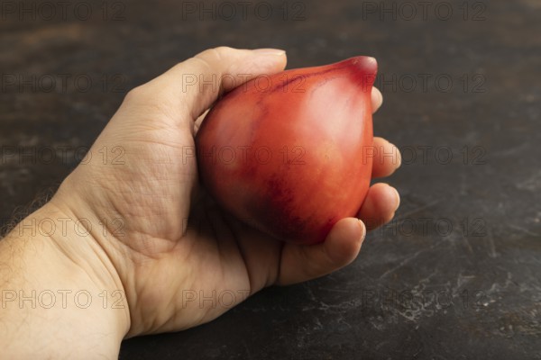 Red Heart shape tomatoes with hand on black concrete background. Side view, copy space. healthy food, vegetable, minimalism. hold