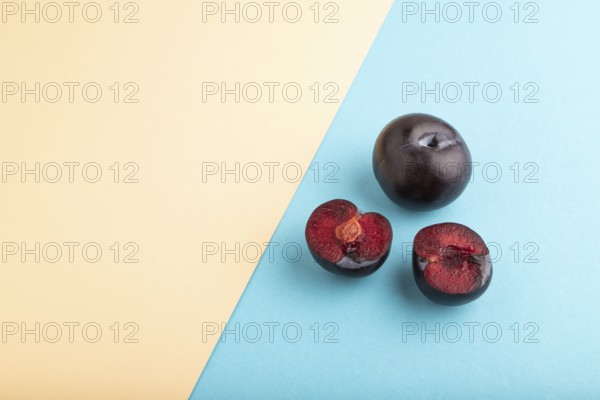 Purple Plum Cut in half on orange and blue pastel paper background. Side view, copy space. healthy food, vegetable, minimalism