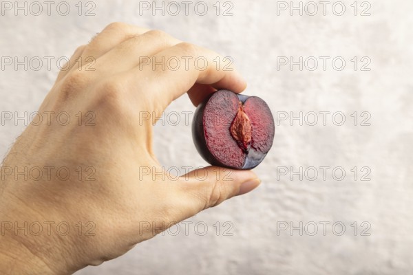 Purple Plum Cut in half with hand on gray concrete background. Side view, close up. healthy food, vegetable, minimalism