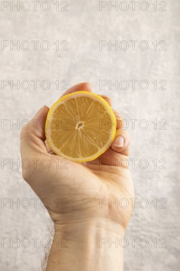 Yellow Lemon Cut in half with hand on gray concrete background. Side view, close up. healthy food, vegetable, minimalism. citrus