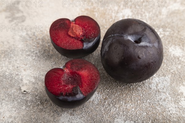 Purple Plum Cut in half on brown concrete background. Side view, close up. healthy food, vegetable, minimalism