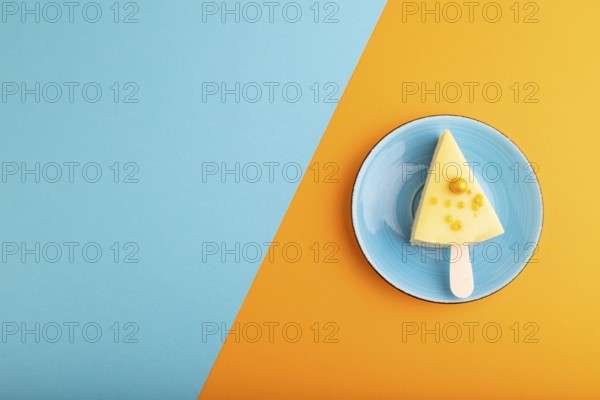 Yellow Cake pop with sprinkles on blue ceramic plate on blue and orange pastel paper background, top view, flat lay, copy space, minimalism