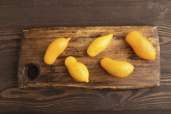 Yellow tomatoes on cutting board on brown wooden background. Top view, copy space, flat lay. healthy food, vegetable, minimalism