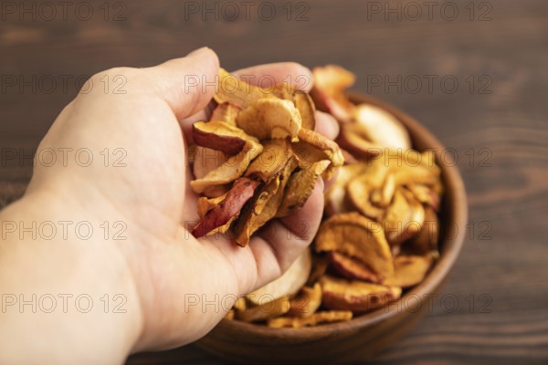Dried Apples in wooden bowl with hand on brown wooden background. Side view, close up, healthy food, minimalism. sweet, selective focus