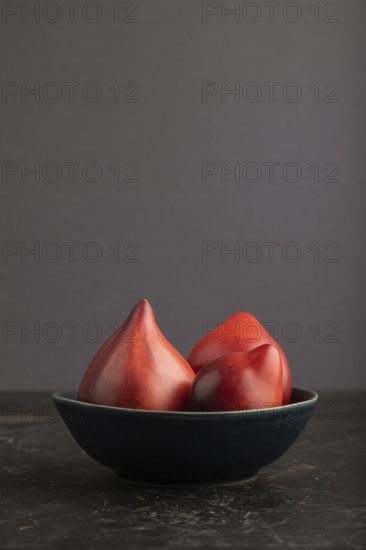 Red Heart shape tomatoes in blue bowl on black concrete background. Side view, copy space. healthy food, vegetable, minimalism, low key