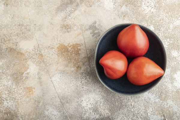 Red Heart shape tomatoes in blue bowl on brown concrete background. Top view, copy space, flat lay. healthy food, vegetable, minimalism