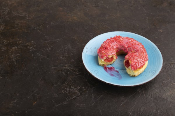 Bitten Pink Donut with sprinkles on blue ceramic plate on black concrete background, side view, copy space, minimalism