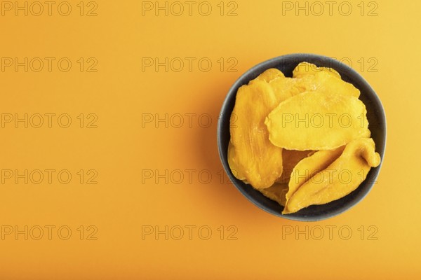 Dried Mango in blue ceramic bowl on orange pastel paper background. Top view, copy space, flat lay. healthy food, minimalism