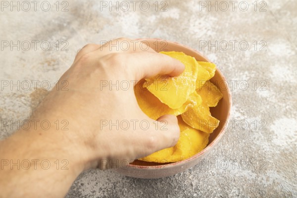 Dried Mango in ceramic bowl with hand on brown concrete background. Side view, close up. healthy food, minimalism