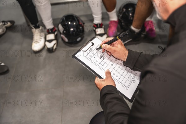 American football coach holding a clipboard, drawing strategies on a field diagram, instructing players in a locker room during a huddle, discussing tactics and game plan