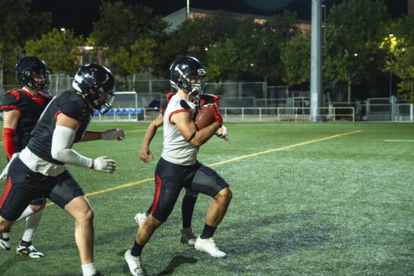 American football player is running with the ball, while teammates are blocking opponents during an intense game on a floodlit artificial turf field under the night sky