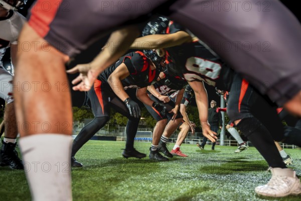 American football players crouched on green artificial turf under stadium lights, lined up for a night scrimmage, focused and ready for intense teamwork and competitive play