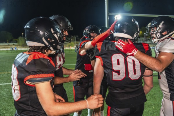 Football teammates huddling on the field under stadium lights at night, celebrating teamwork and unity after a play, showing determination, camaraderie, and competitive spirit