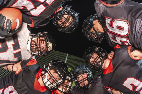 American football players wearing helmets and uniforms. Gathering in a huddle. Sharing a moment of intense communication and teamwork on the stadium field at night. Symbolizing unity and game strategy