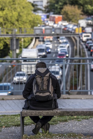 Man sitting on a bench, looking at the traffic jam on the A40 motorway, Ruhrschnellweg, in the city passage of Essen, at Europaplatz, entrance to the Ruhrschnellweg tunnel, North Rhine-Westphalia, Germany