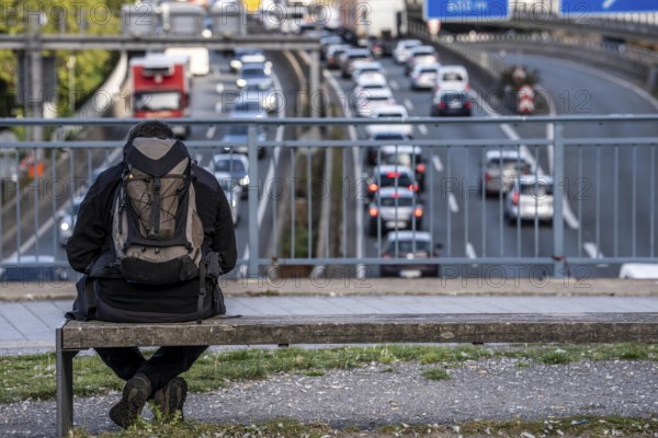 Man sitting on a bench, looking at the traffic jam on the A40 motorway, Ruhrschnellweg, in the city passage of Essen, at Europaplatz, entrance to the Ruhrschnellweg tunnel, North Rhine-Westphalia, Germany