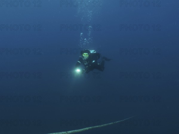 Ein Taucher mit Lampe steigt aus der dunklen Unterwasserwelt auf, einem Seil folgend. Tauchplatz Wrack der Giuseppe Dezza, Pula, Kroatien, Mittelmeer
