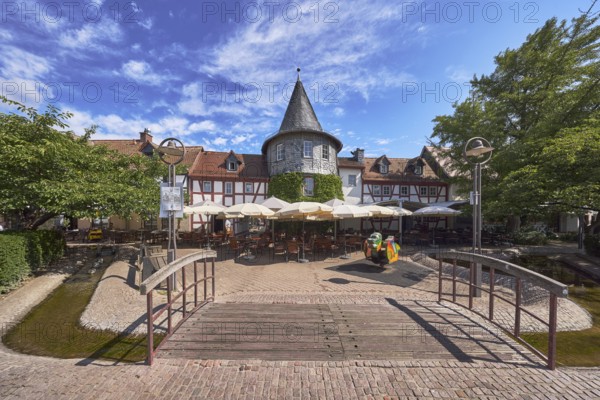 Fachwerkhäuser, Turm, Häuserzeile, Fußgängerbrücke, Holzbrücke, hölzern, Altstadt, historische Gebäude, Gehweg aus Klinker, Pflastersteine, Restaurant Zum Türmchen, Außenbereich einer Gastronomie mit Sonnenschirmen, Tischen und Stühlen, blauer Himmel, Cumuluswolken, Cirrostratuswolken, Platz am Untertor, Burggrabenstraße, Hofheim am Taunus, Main-Taunus-Kreis, Hessen, Deutschland