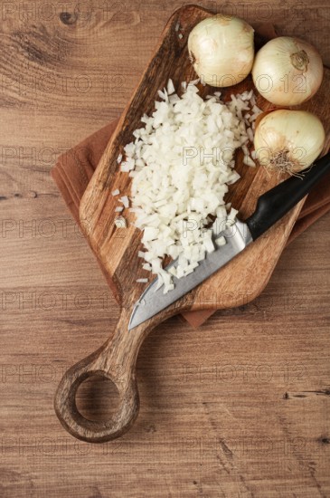 Finely chopped onion on a chopping board with a knife, wooden table, top view, no people