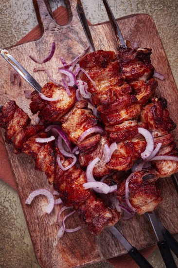 Pork kebab on skewers, with red onion, on a wooden chopping board, close-up, top view