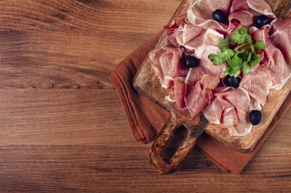 Sliced prosciutto, on a cutting board, with olives and herbs, snack, breakfast, no people