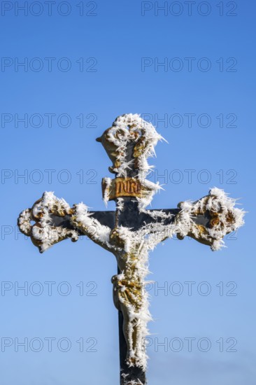 Crucifix with hoarfrost in front of blue sky at sunshine in winter, Bavaria, Germany
