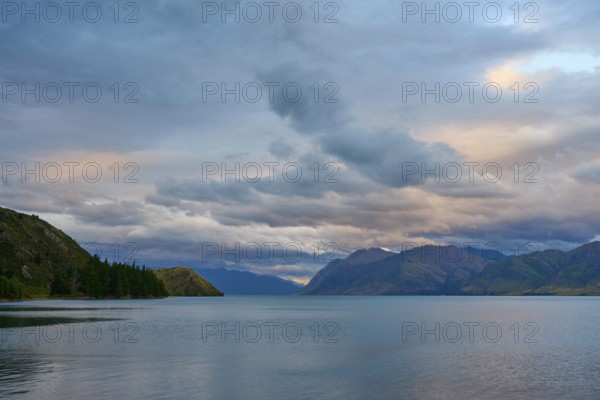 Friedlicher See mit Bergpanorama und bewölktem Himmel kurz vor Sonnenuntergang, Lake Hawea, Hawea, Otago, Südinsel, Neuseeland