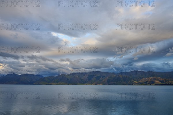 Stilles Gewässer vor bergiger Landschaft und dramatischem Himmel in der Dämmerung, Lake Hawea, Hawea, Otago, Südinsel, Neuseeland
