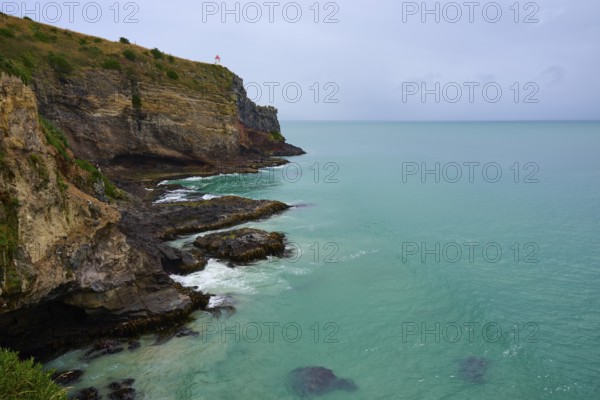 Dramatische Küstenlandschaft mit steilen Klippen Leuchturm und grünlich-blauem Meer unter einem bewölkten Himmel, Waiwhakaheke Seabird Lookout, Taiaroa Head, Harington Point, Dunedin, Otago, Südinsel, Neuseeland