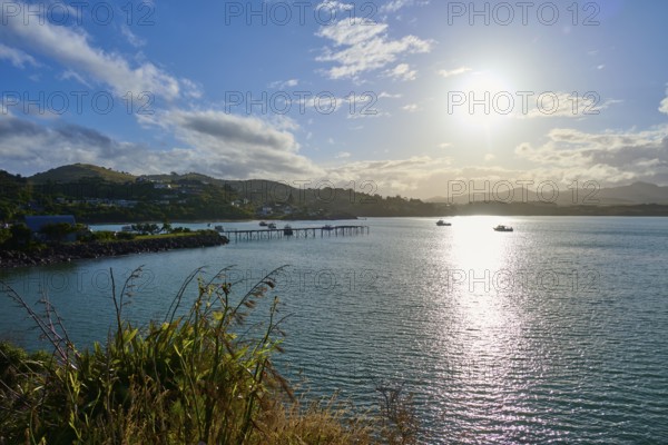 Das Sonnenlicht reflektiert auf dem Meer mit Booten und einem Pier, Moeraki, Hampden, North Otago, Südinsel, Neuseeland