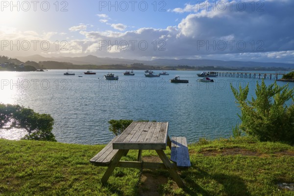 Ein Picknicktisch auf einem Hügel mit Blick auf Boote im Wasser, Moeraki, Hampden, North Otago, Südinsel, Neuseeland