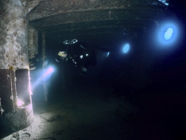 Diver exploring a dark wreck underwater, illuminated by torchlight. Dive site wreck of the Vis, Pula, Croatia, Mediterranean Sea