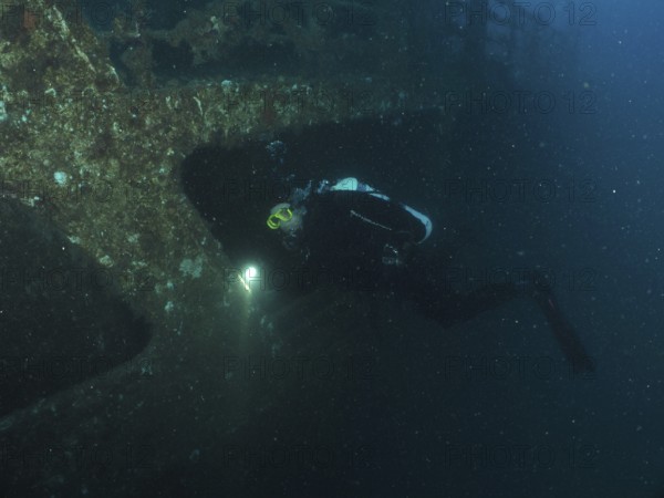 Diver examines a shipwreck with a lamp in the dark. Dive site wreck of the Vis, Pula, Croatia, Mediterranean Sea